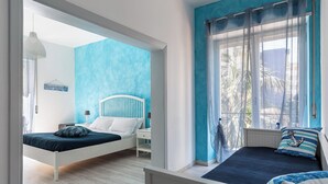 A bedroom with a bed, bedside tables, a hanging lamp, and a window with curtains. - Quadruple room at 25 rimini street within walking distance of serapo beach VOLARE (Gaeta)