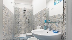 A bathroom with patterned tiles, a glass shower enclosure, a white sink, and a toilet. - Quadruple room at 25 rimini street within walking distance of serapo beach VOLARE (Gaeta)