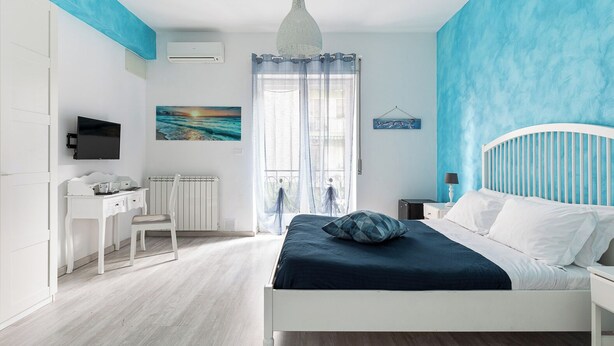 A bedroom with a bed, a desk, a chair, a television, and a window with curtains. - Quadruple room at 25 rimini street within walking distance of serapo beach VOLARE (Gaeta)