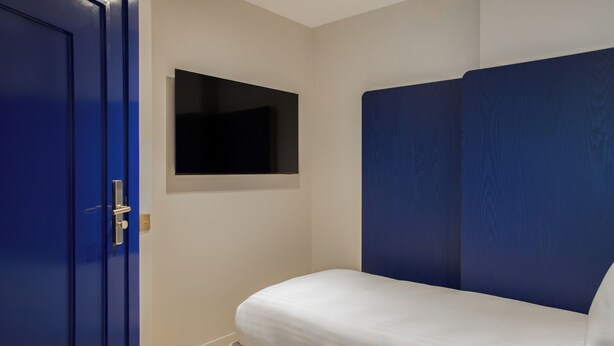 A bedroom with a bed, a blue door, and a mounted television.