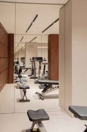 A gym with exercise equipment, a mirrored wall, and a wooden panel wall. - Hotel Leev Miromesnil (Paris)