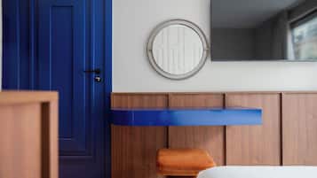 Une pièce avec une porte bleue, un miroir rond doté d’un cadre circulaire, une armoire en bois et un banc en bois.