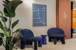 A modern interior with two blue chairs, a blue stool, and a wall-mounted abstract artwork. - Hotel Leev Miromesnil (Paris)