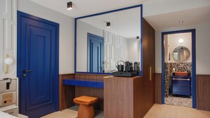 A modern bathroom with a blue door, a wooden vanity, a round mirror, and a small stool.