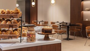 A bakery display with pastries and a cake, tables and chairs in a cafe setting.