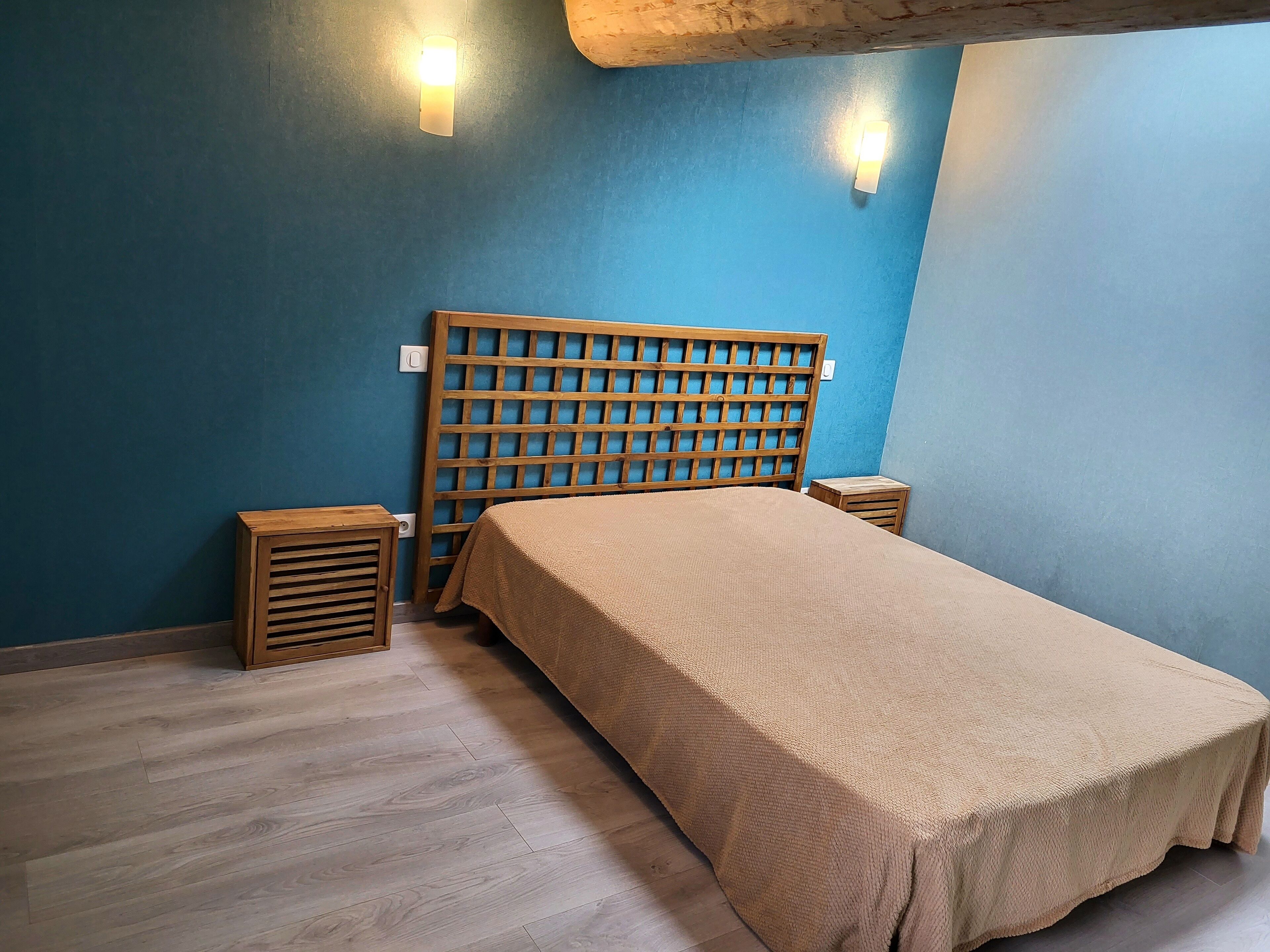 A bedroom with a wooden headboard, a bed with a beige bedspread, two nightstands, and a small wooden stool.