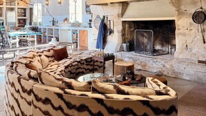 A cozy living room with a large, patterned sofa, a fireplace, and a dining area with a table and chairs. - Bastide with garden and swimming pool 10 minutes from Saint Rémy de Provence (Eyragues)