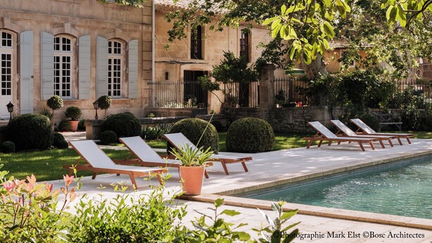 A poolside area with lounge chairs, a swimming pool, and a building with arched windows and shutters. - Bastide with garden and swimming pool 10 minutes from Saint Rémy de Provence (Eyragues)