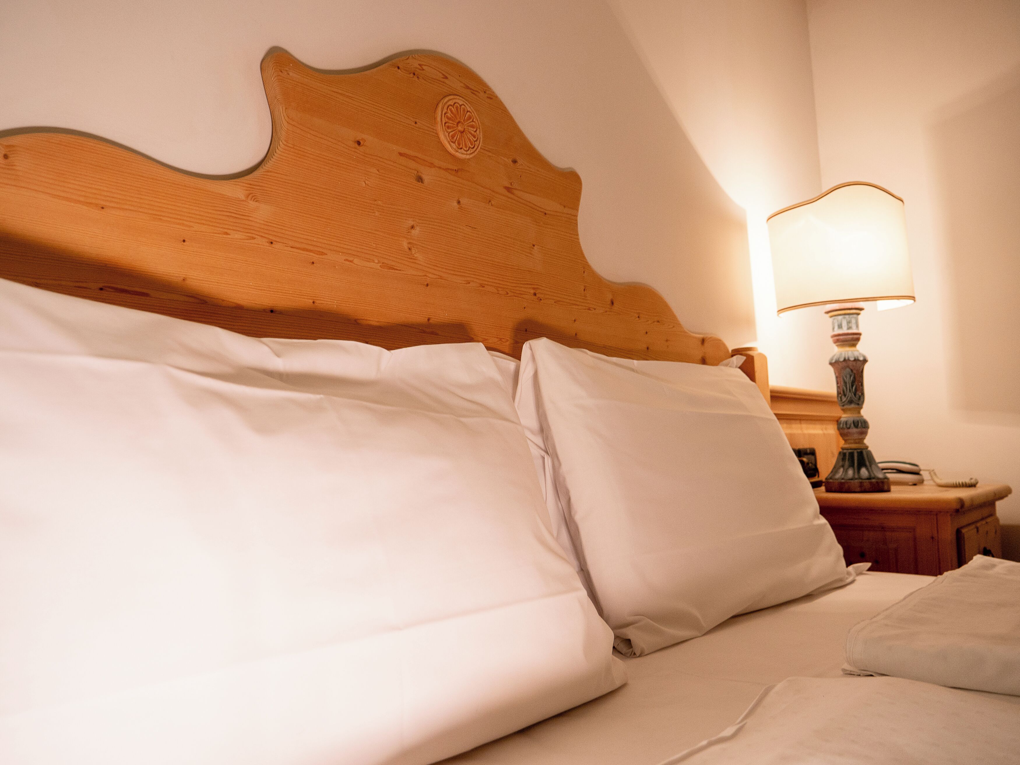Ein ordentlich bezogenes Bett mit weißen Leinen und einem Holzkopfstück.