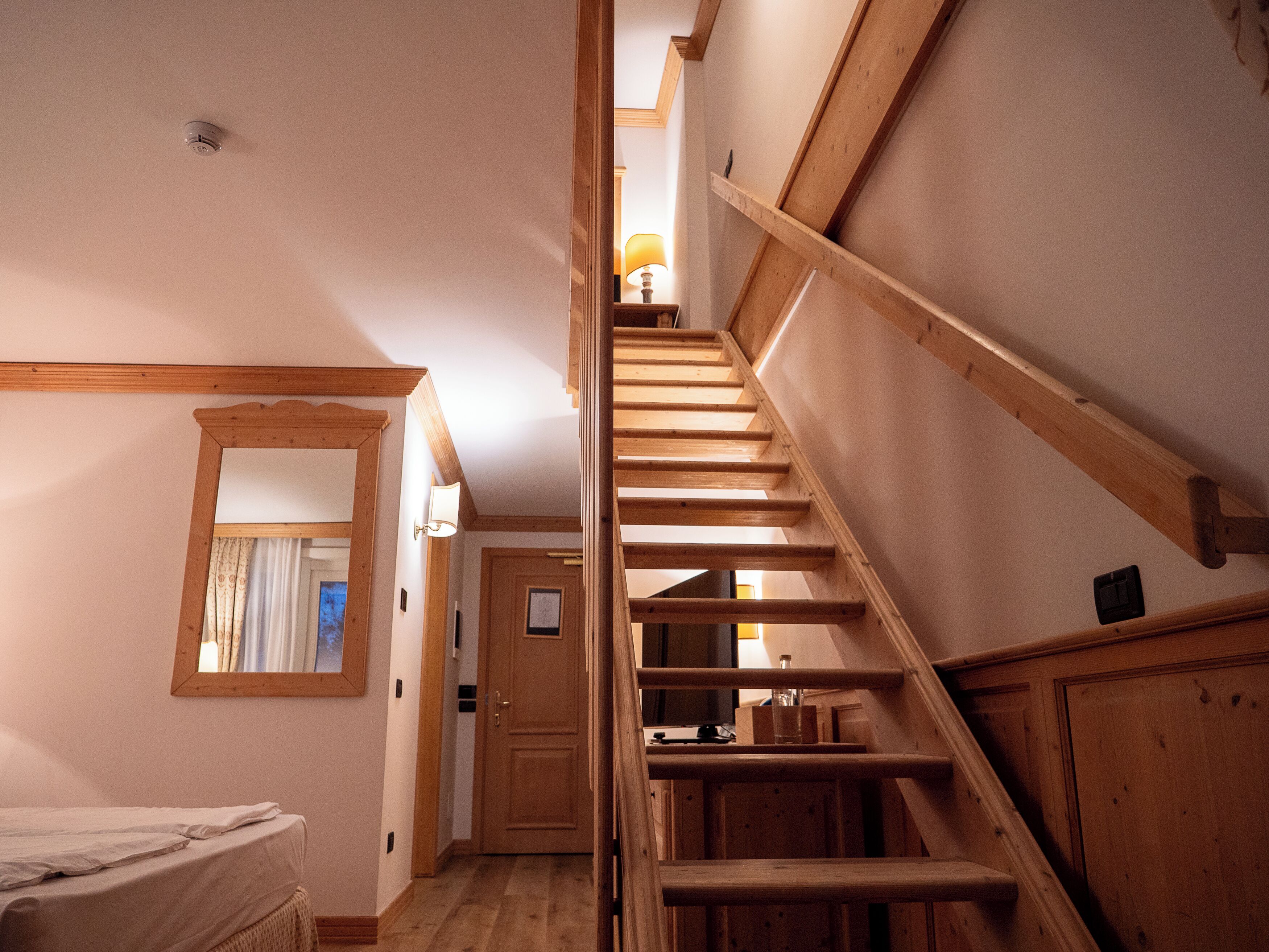 Una escalera de madera en una habitación con cama y puerta.