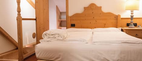 A hotel room with a wooden headboard, a bed with neatly folded white linens, a nightstand with a lamp, and a wooden staircase.