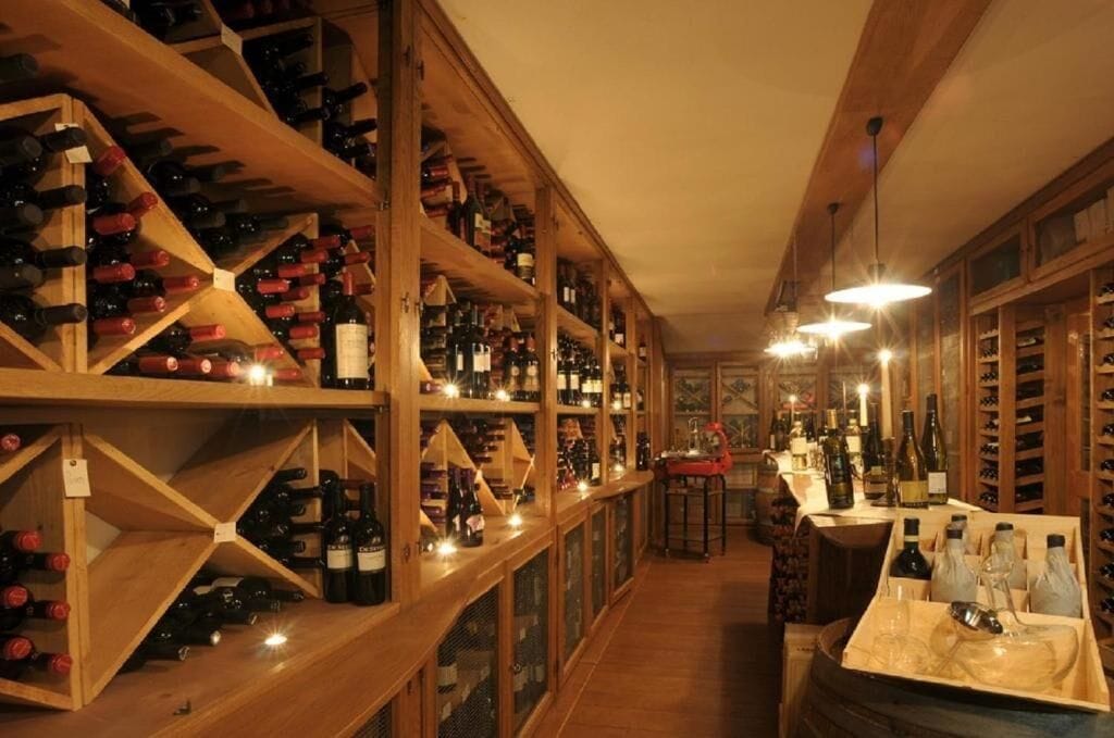 A wine cellar with wooden shelves and racks, a bar area with bottles and glasses, and a warm, dimly lit ambiance.