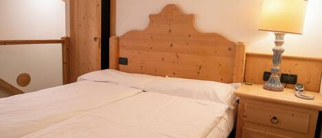 Una cama de madera con ropa blanca, una lámpara de noche y una mesita de noche de madera con un cajón.