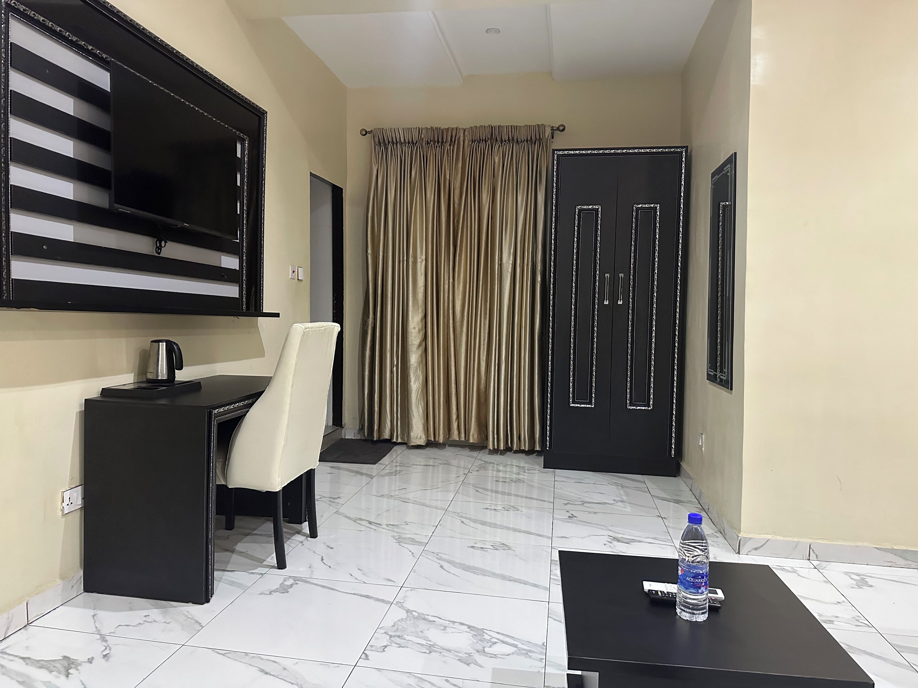 Une chambre d’hôtel équipée d’un bureau, d’une chaise, d’un grand téléviseur à écran plat, d’une bouteille d’eau sur une table et d’une armoire.