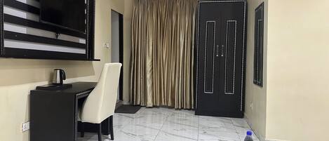 Une chambre d’hôtel équipée d’un bureau, d’une chaise, d’un grand téléviseur à écran plat, d’une bouteille d’eau sur une table et d’une armoire.