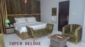A hotel room with a large bed, two armchairs, a small table, a nightstand, a lamp, and a mirror. - De Lords Resort Hotel & Suites (Lagos)