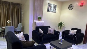 A living room with two black sofas, a coffee table, a small table with chairs, a potted plant, and a painting on the wall. - De Lords Resort Hotel & Suites (Lagos)