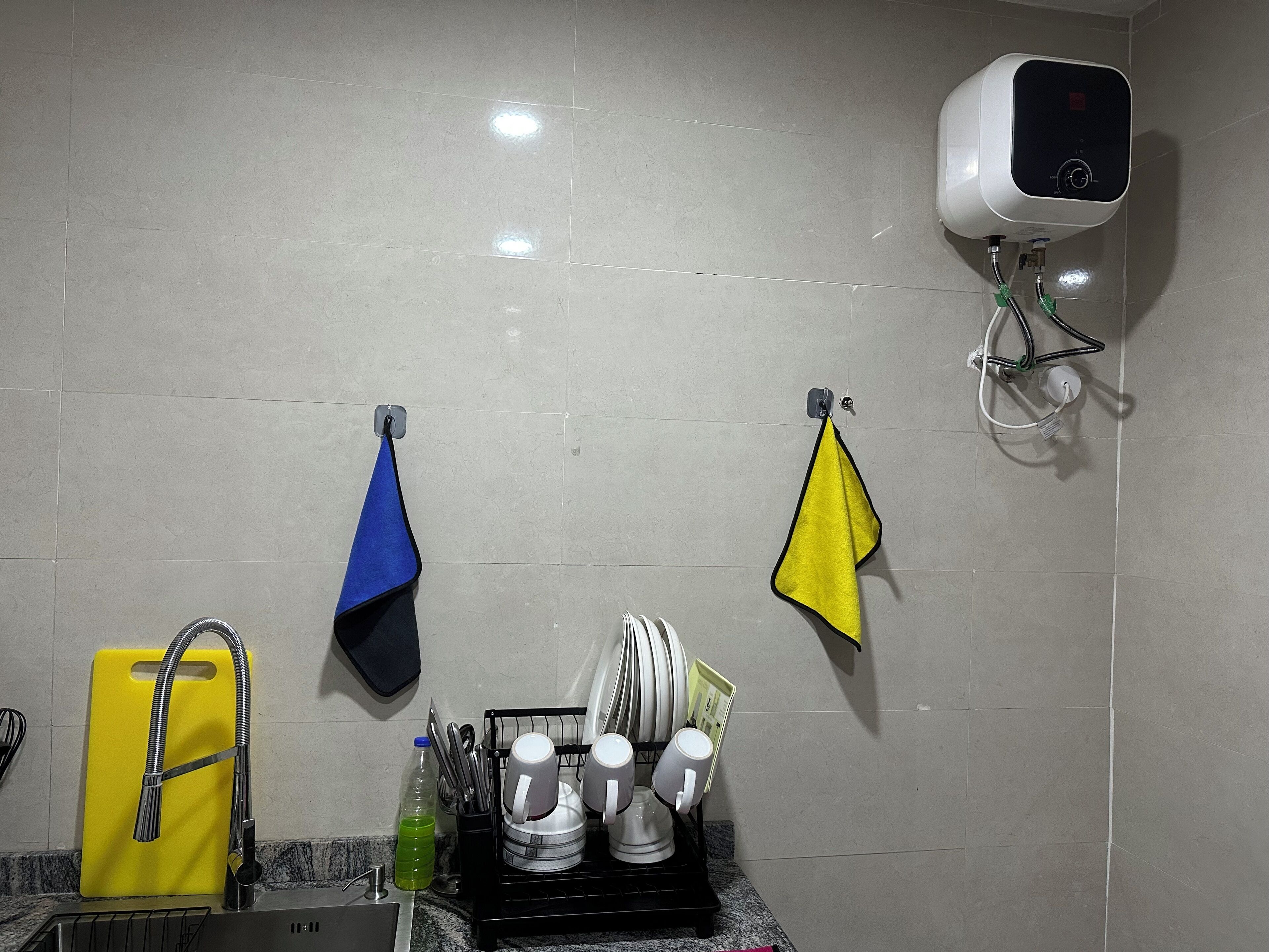 A kitchen with a dish rack, a yellow towel, a blue towel, and a white towel hanging on the wall.