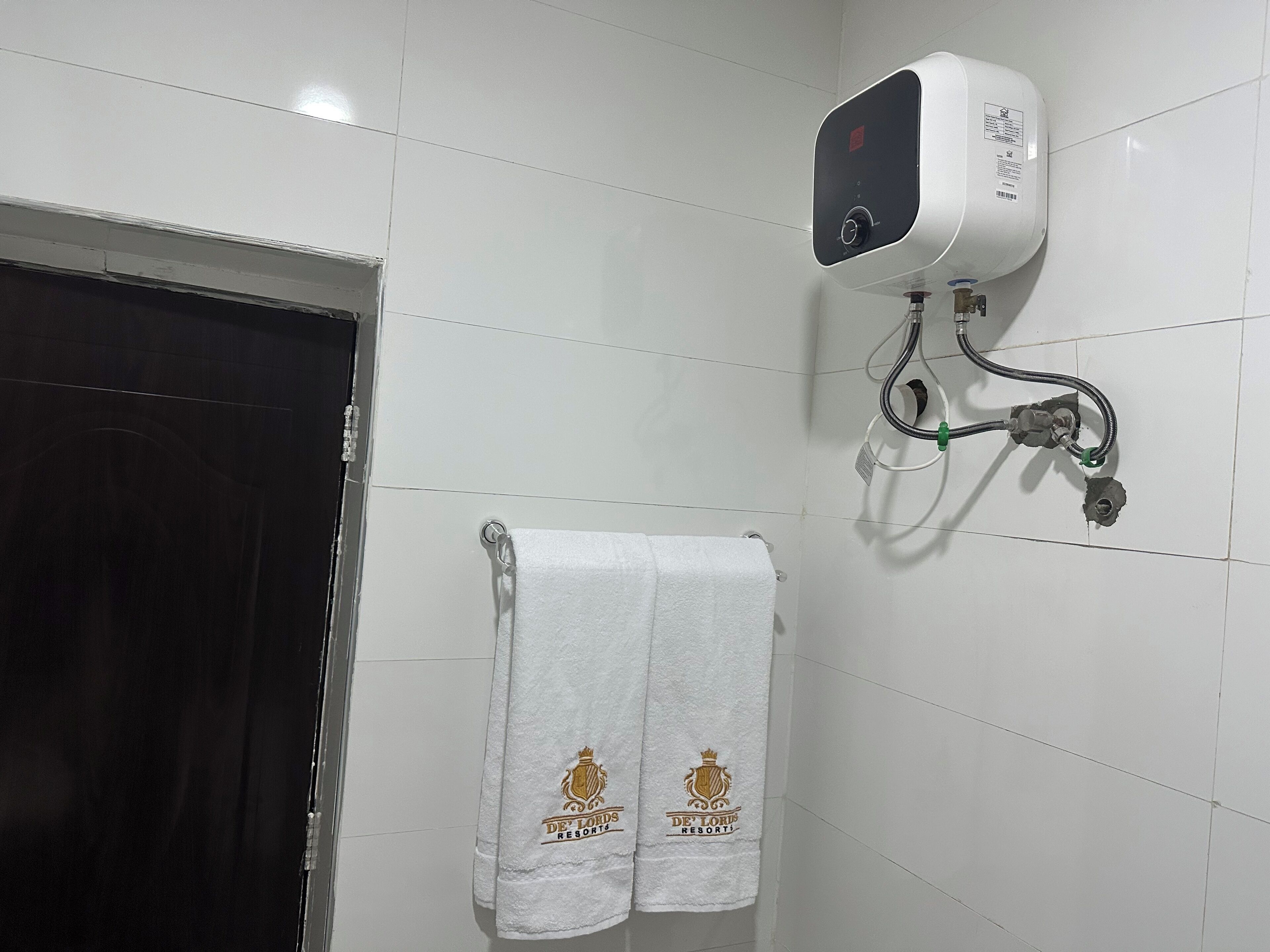 A bathroom with white tiled walls, a white towel hanging on a rack, and a water heater mounted on the wall.