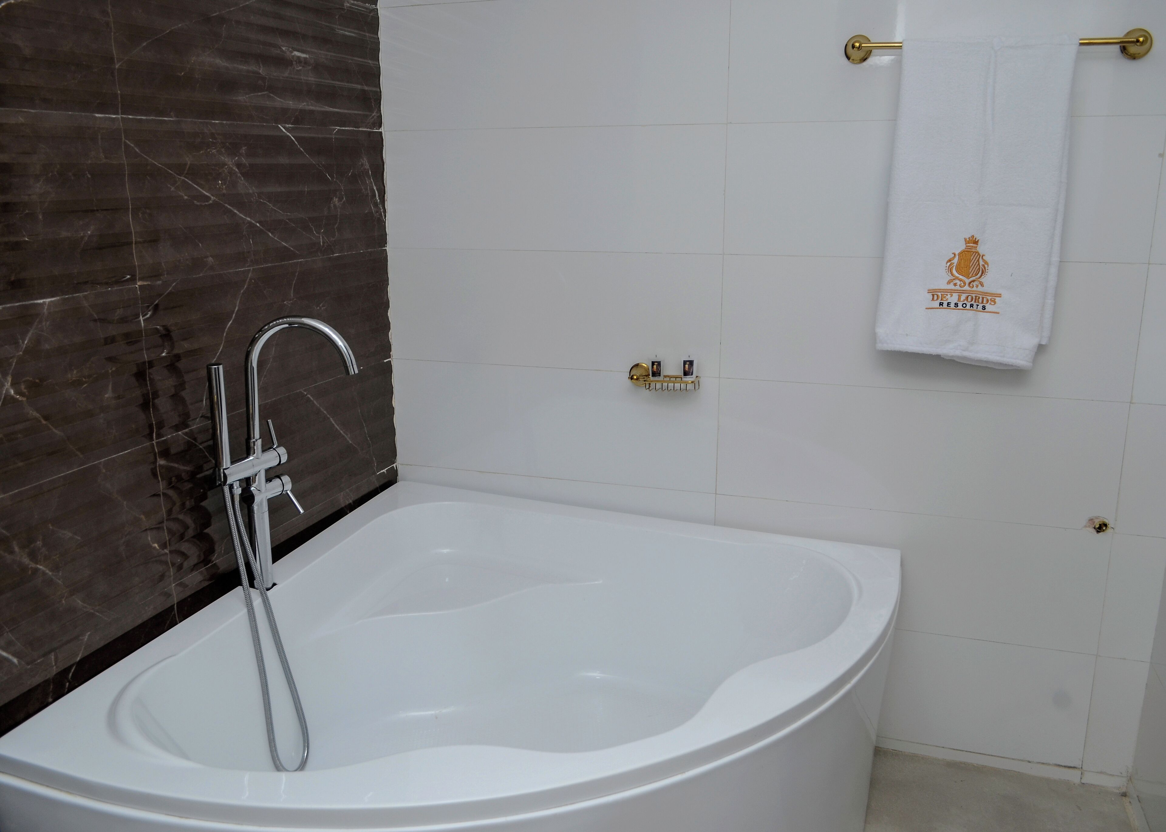 Un baño moderno con una bañera independiente, una pared de mármol, un perchero con una toalla y un aro para toallas dorado.