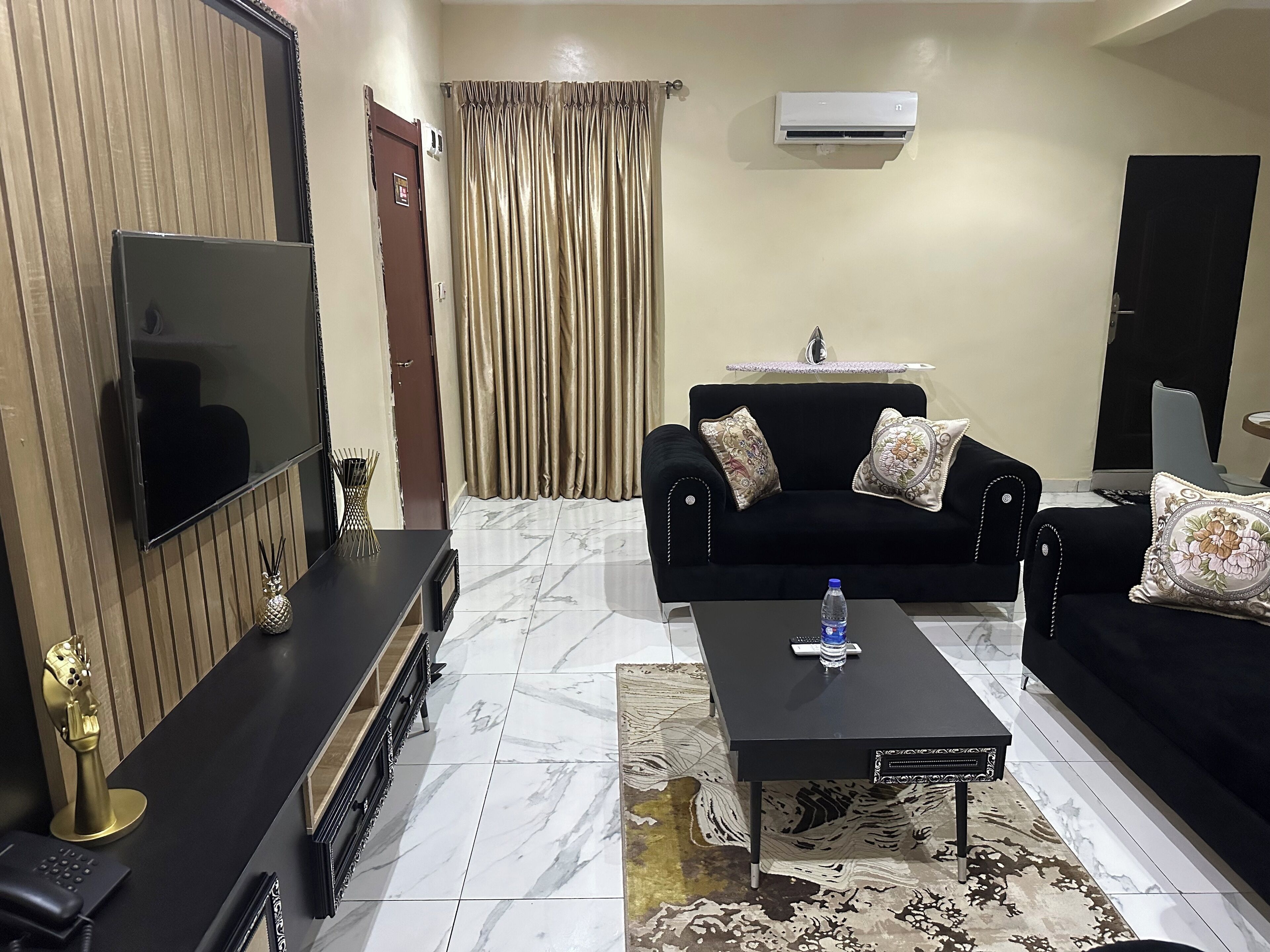 A living room with a black sofa, a coffee table, a TV, and a patterned rug.