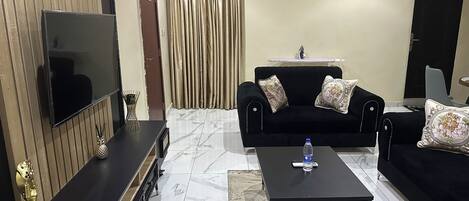 A living room with a black sofa, a coffee table, a TV, and a patterned rug.