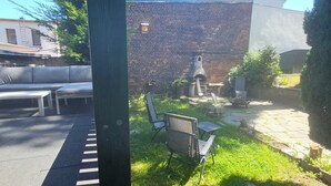 Un pati amb mur de maó, una barbacoa, un banc de fusta i un sofà.