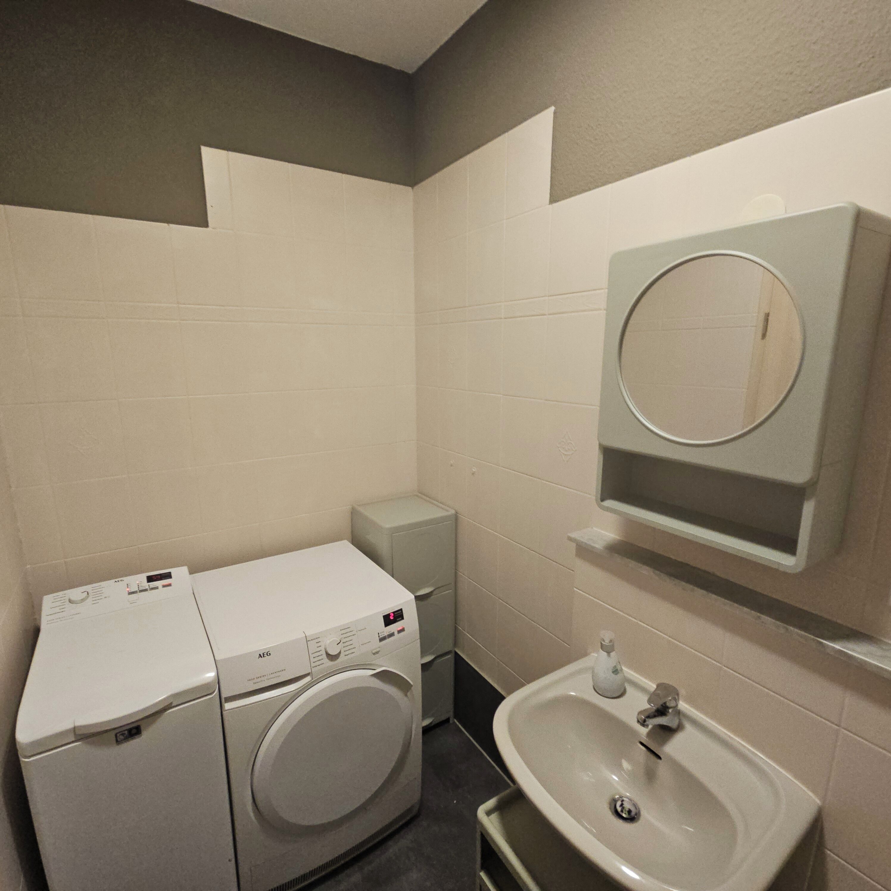 Ein kleines Badezimmer mit Waschmaschine, Waschbecken und Spiegel.