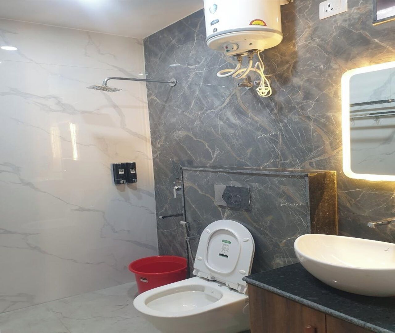 A bathroom with a toilet, a sink, a showerhead, and a marble wall.