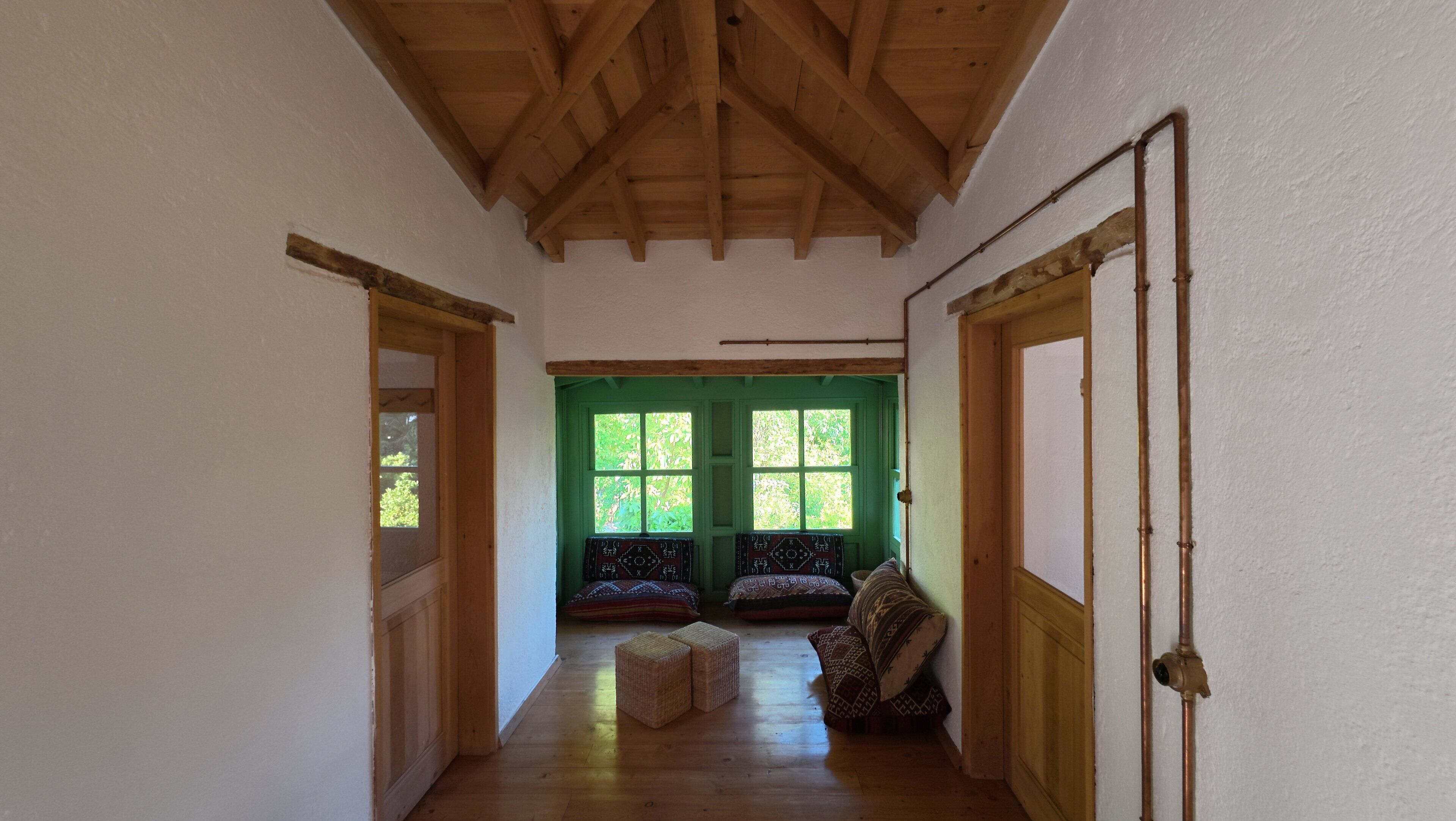 A hallway with wooden beams, a green door, and a window with a view of trees.