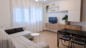 A modern living room with a sofa, a dining table with chairs, a TV on a wooden cabinet, and a plant. - Casa cañaveral     . (Conil de la Frontera)