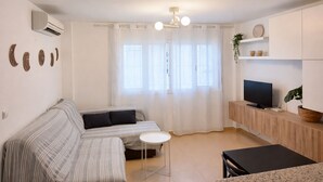 A modern living room with a sofa, a TV, a small table, and a ceiling fan. - Casa cañaveral     . (Conil de la Frontera)