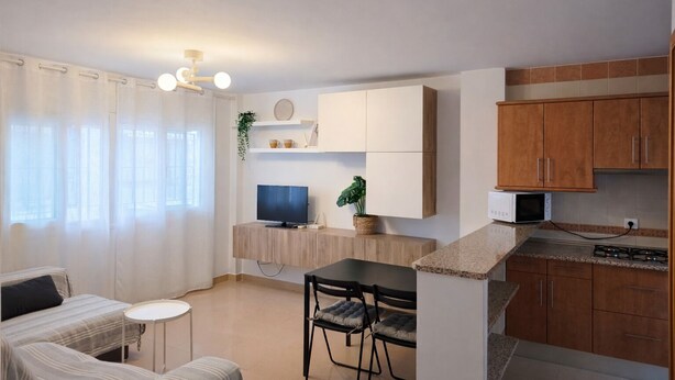 A compact living space with a kitchenette, a dining area with a table and chairs, a TV, and a window with curtains. - Casa cañaveral     . (Conil de la Frontera)
