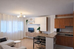 A compact living space with a kitchenette, a dining area with a table and chairs, a TV, and a window with curtains. - Casa cañaveral     . (Conil de la Frontera)