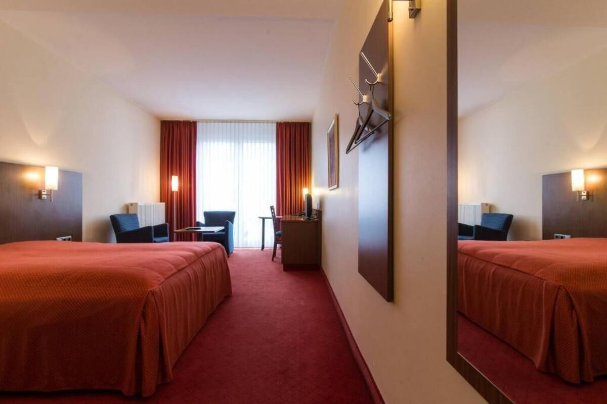 Een hotelkamer met twee bedden, een bureau, een stoel, een spiegel en uitzicht op de straat.