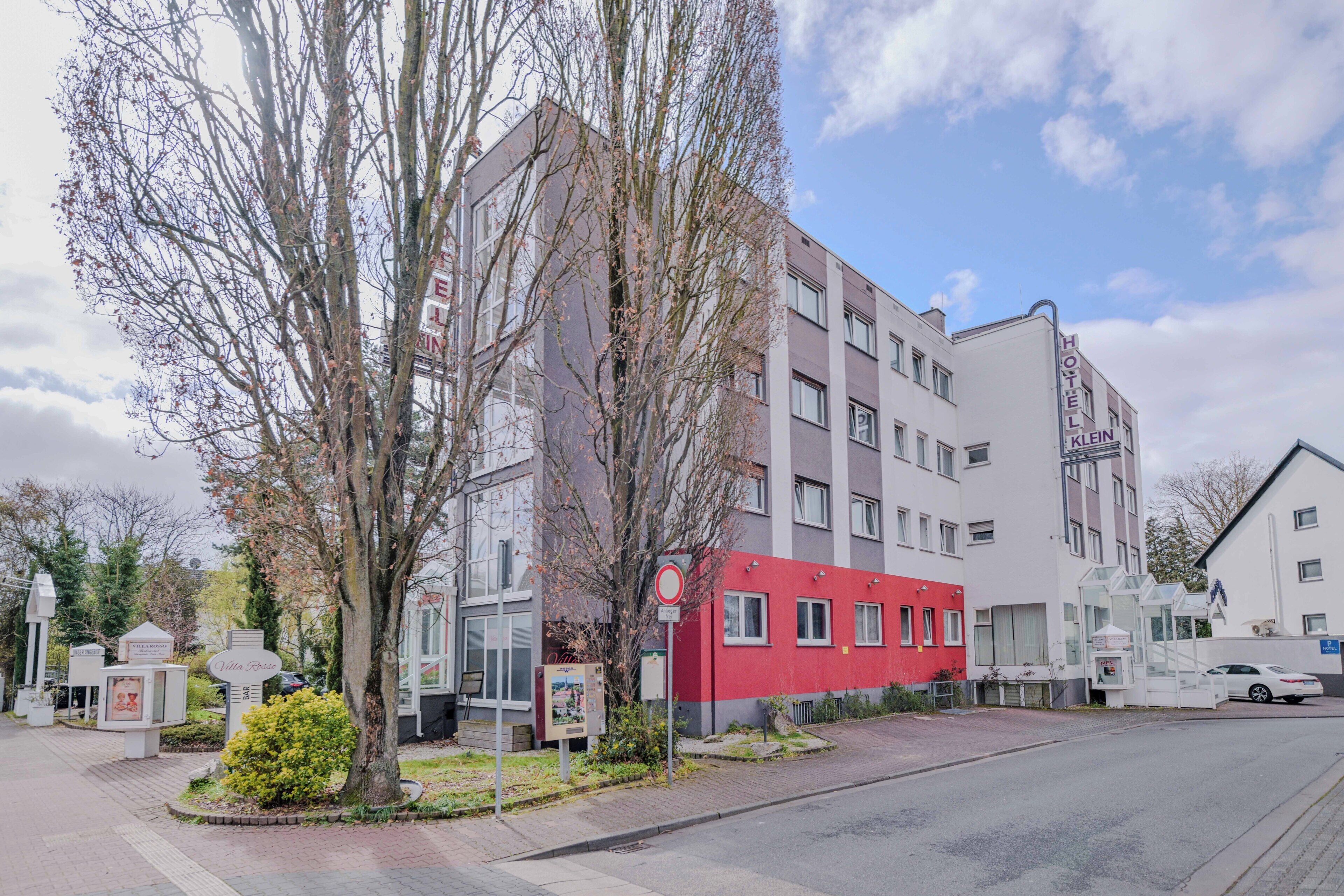 Un hotel de varios pisos con fachada roja y blanca, ubicado en una calle bajo un cielo despejado.