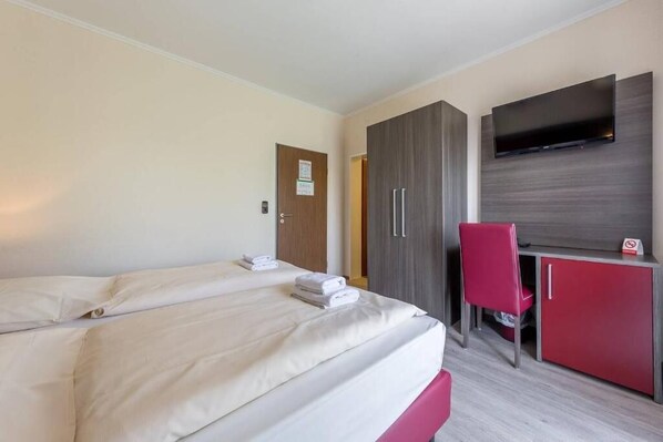 Ein Hotelzimmer mit zwei Betten, einem Schreibtisch, einem Fernseher und einem roten Sessel.