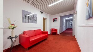 A hallway with a red carpet, a red sofa, a red chair, and a small table with a vase of flowers. - Hotel Klein (Frankfurt)