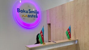 Vastaanottotiski, jonka yläpuolella on neonvalomainos, jossa lukee ”Baku Smile Hostel”, ja sen päällä on kaksi lippua.