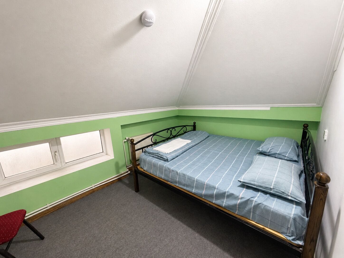 A single bed with a metal frame and a blue striped bedspread in a room with green walls and a white ceiling.