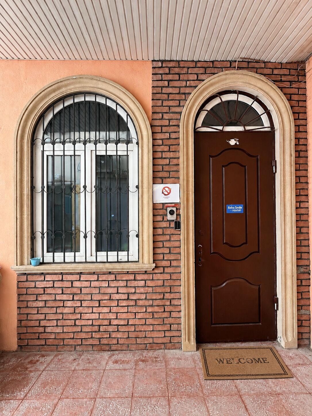 A hotel entrance with a brown door, a welcome mat, and a no smoking sign.