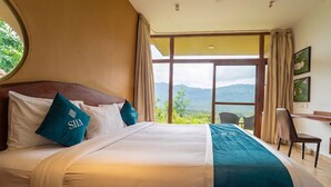 Ein Hotelzimmer mit einem großen Bett, Blick ins Freie und einem Schreibtisch mit Stuhl.