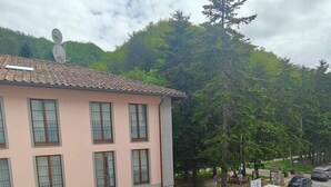 Un immeuble à plusieurs étages, avec un toit recouvert de tuiles, des voitures garées et une colline verdoyante en arrière-plan.