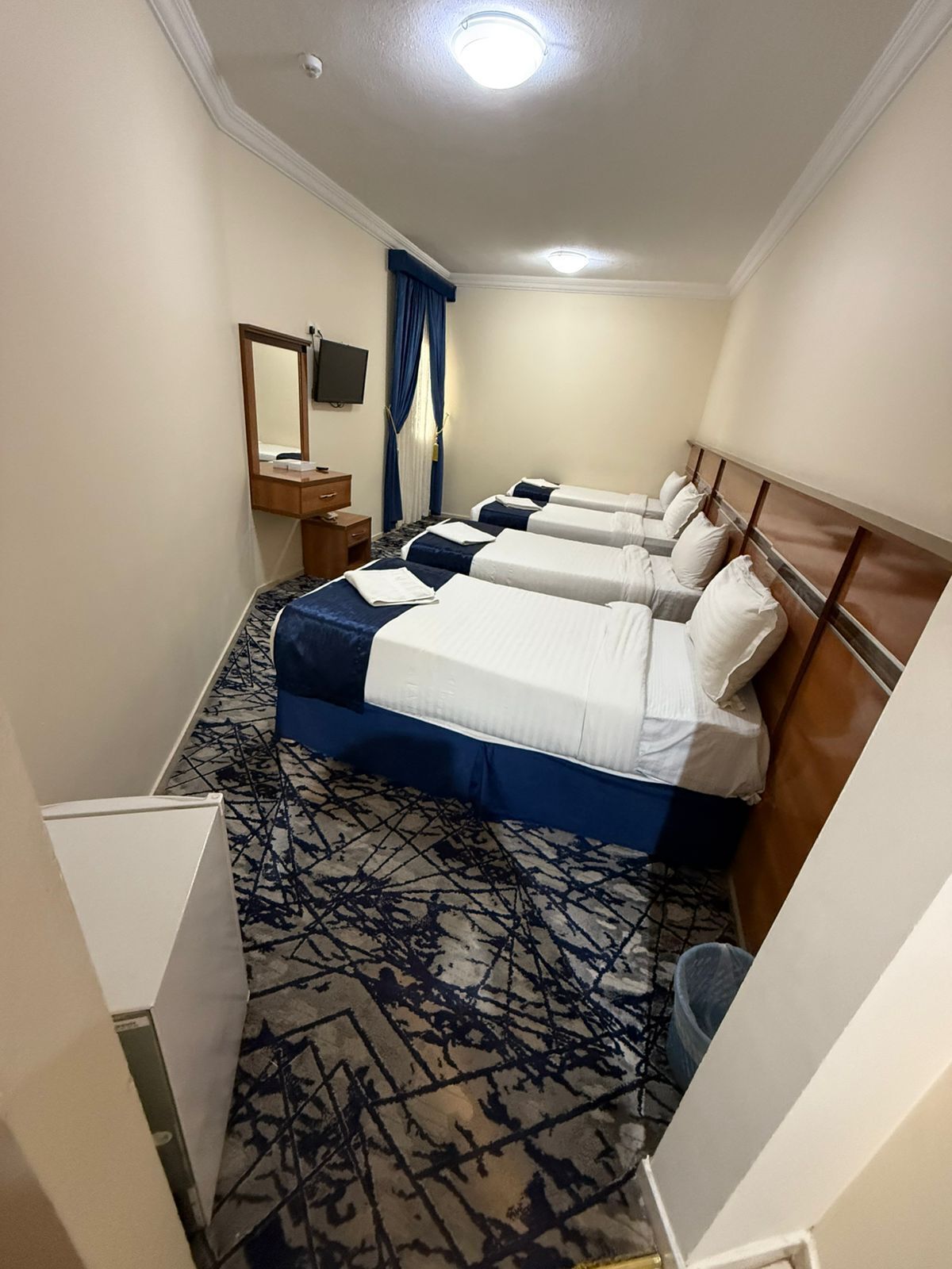 A hotel room with three beds, a desk, a mirror, and a television.