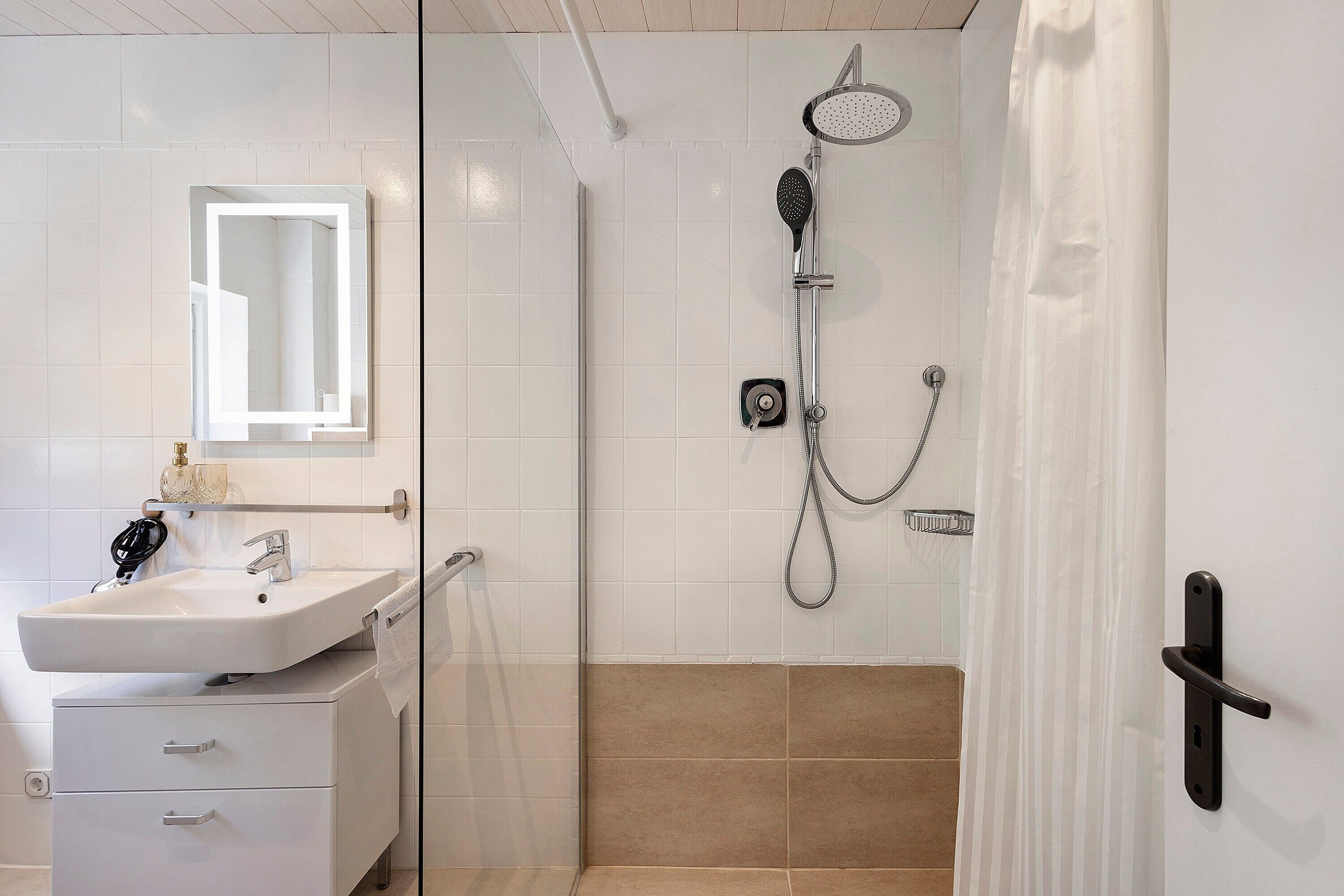 Une salle de bain avec un lavabo, un miroir, une douche et une porte dotée d’une poignée.