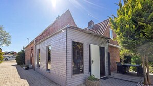 A small, single-story house with a brick chimney, a wooden exterior, and a paved driveway. - Luxury Holiday Home with Sauna, Fireplace, Pool Table, Garden, BBQ & Plenty of Space to Relax (Klein Rönnau)