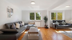 A modern living room with a sectional sofa, a coffee table, and a large window providing natural light. - Luxury Holiday Home with Sauna, Fireplace, Pool Table, Garden, BBQ & Plenty of Space to Relax (Klein Rönnau)
