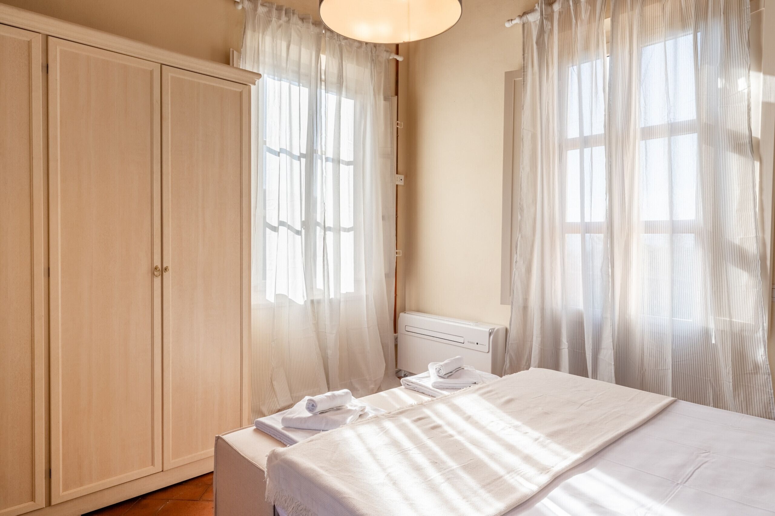 A bedroom with a bed, a wardrobe, and sheer curtains.