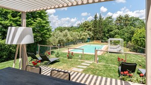 Uma área externa coberta com piscina, espreguiçadeiras e um pérgola.