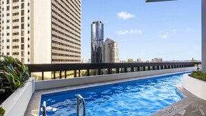 Piscina no terraço com vista para edifícios altos, guarda-corpo de metal e céu claro.
